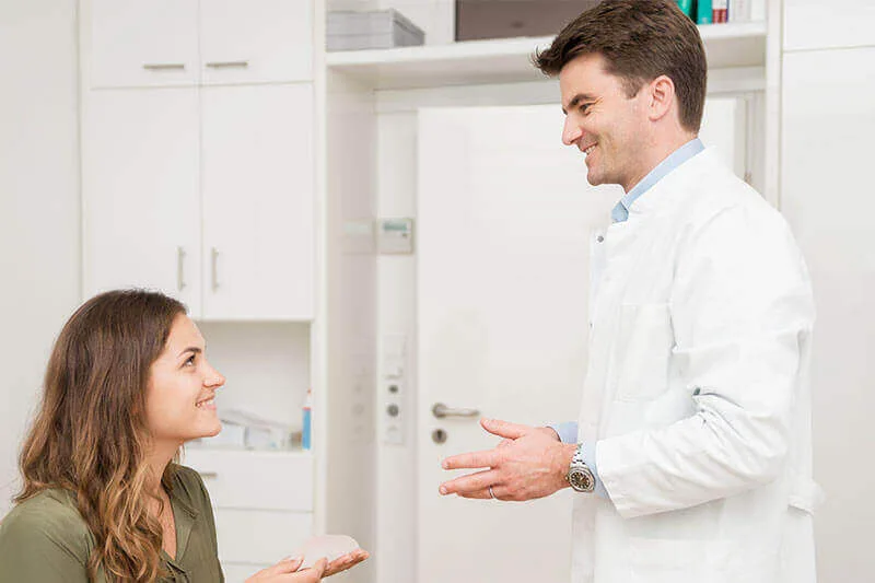Beratungsgespräch mit einer Patientin, die ein Silikonimplantat in den Händen hält.